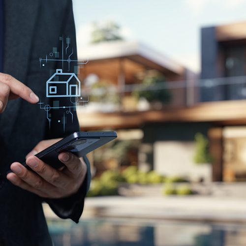 A professional in a suit using a smartphone with a house icon, representing modern technology in the real estate business for buying and selling properties.