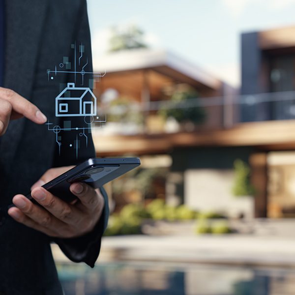 A professional in a suit using a smartphone with a house icon, representing modern technology in the real estate business for buying and selling properties.